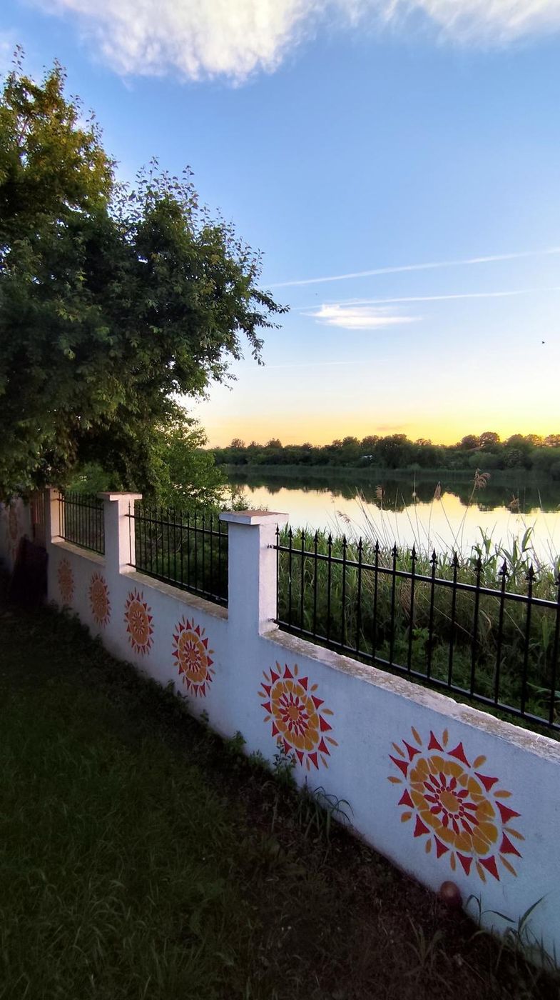 Apus de soare reflectat în lac, lângă gardul pictat cu sori